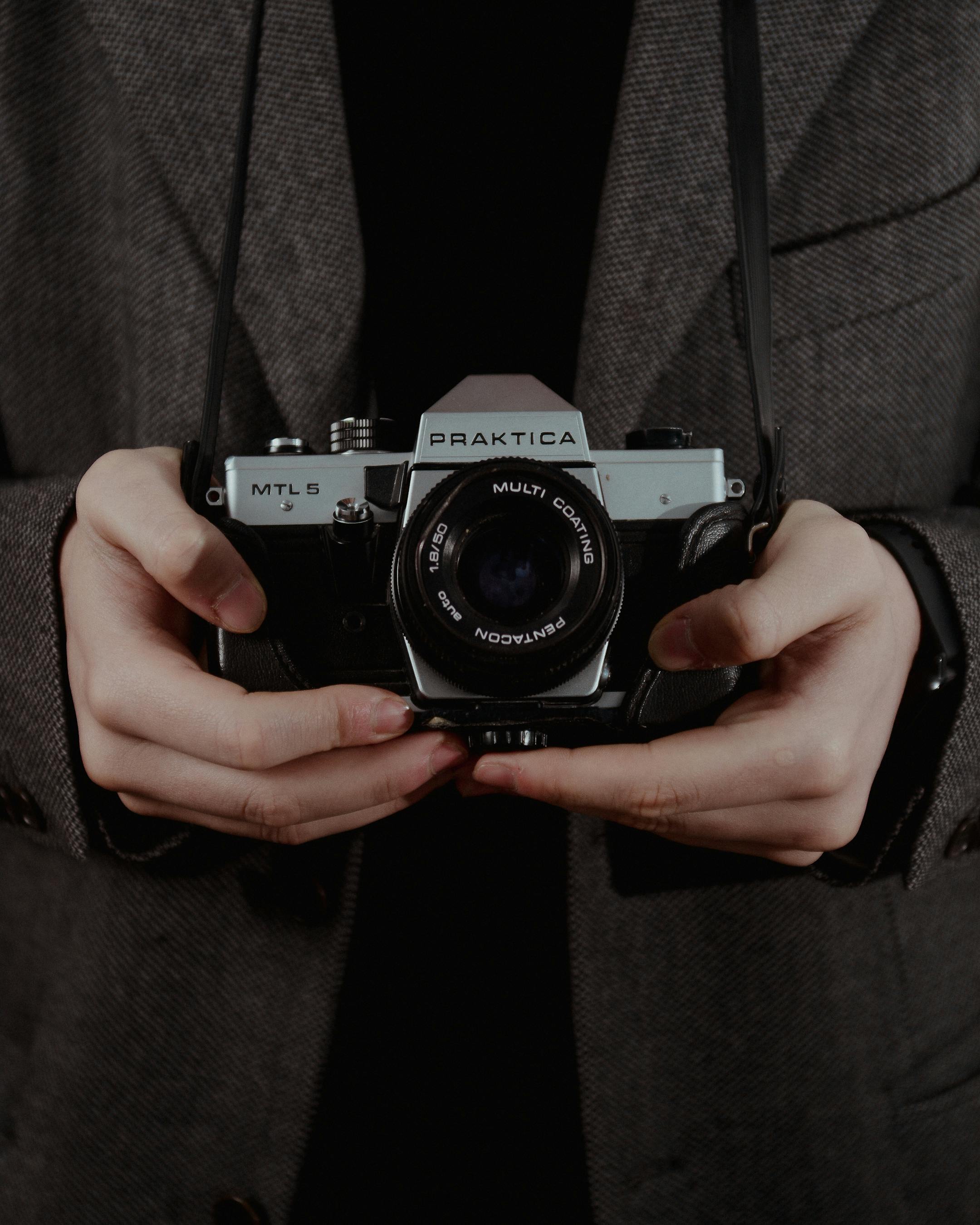 Close-up of hands holding a vintage Praktica camera in a classic setting.
