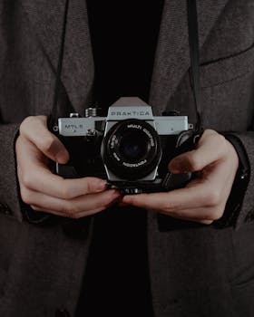 Close-up of hands holding a vintage Praktica camera in a classic setting.