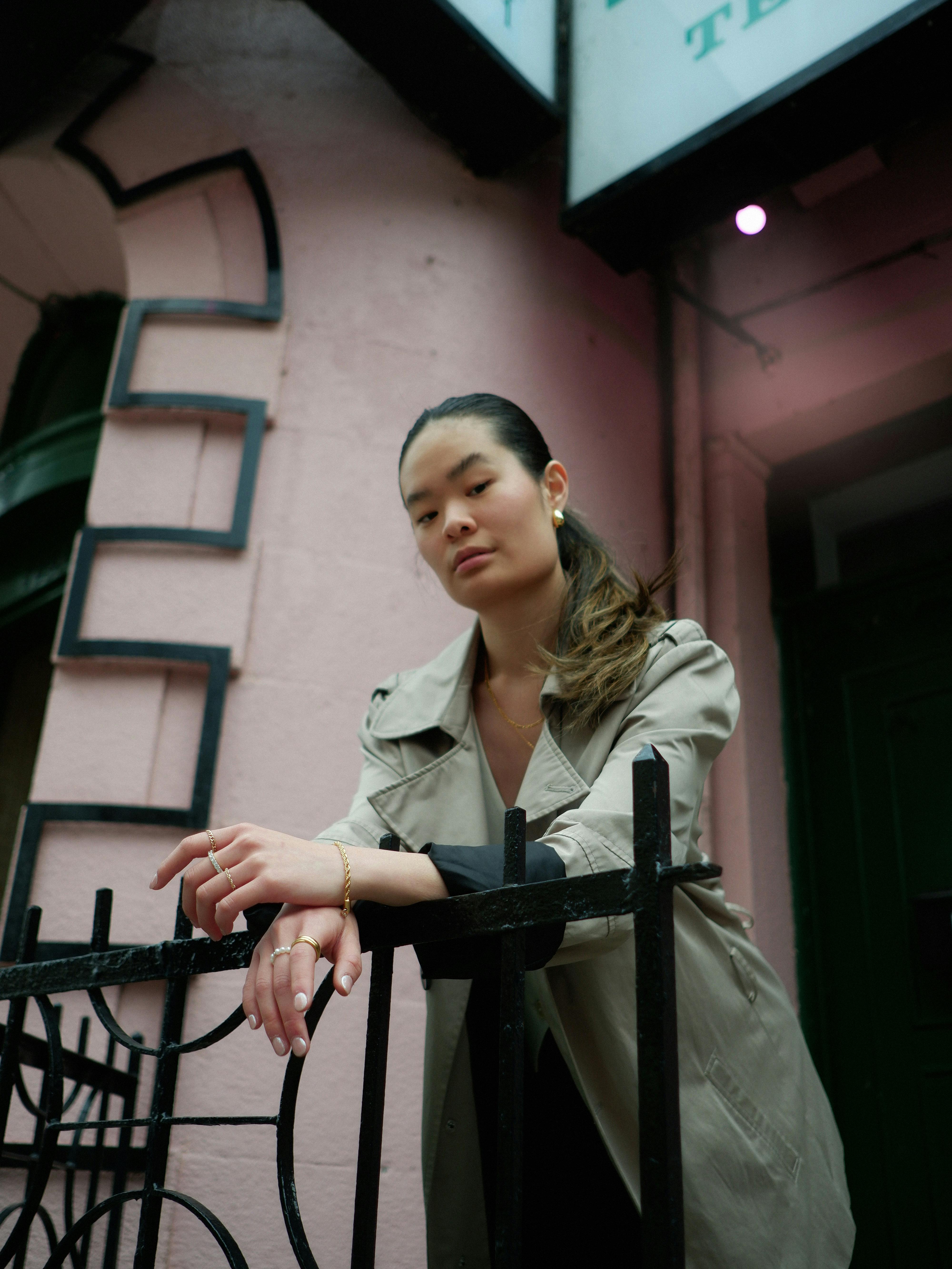 Asian woman in a beige coat posing by a metal banister in Montréal's urban environment.