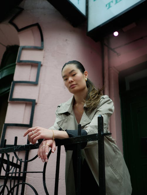A woman leaning on a railing in front of a pink building