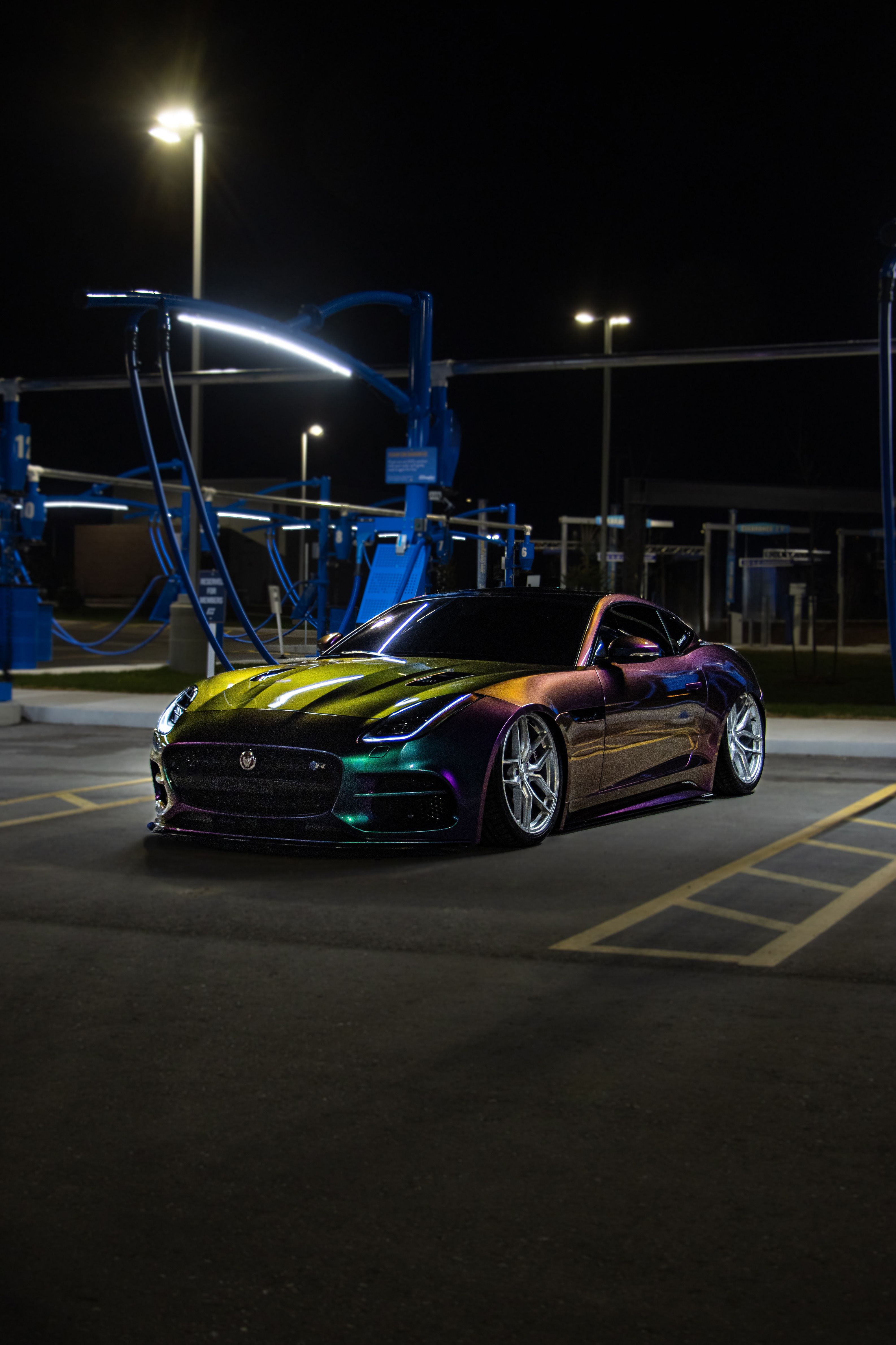 Vibrant sports car with multicolor finish in a well-lit urban area by night.