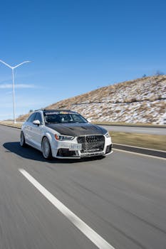 A high-performance silver car speeding on an empty road with clear blue skies above, showcasing speed and design.