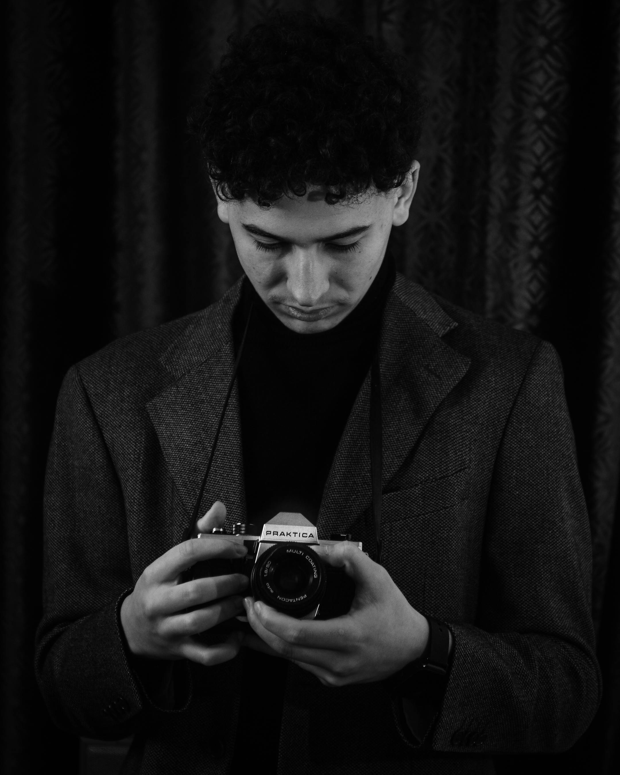 A young man in a suit examines a vintage camera in a black and white portrait, evoking a timeless feel.