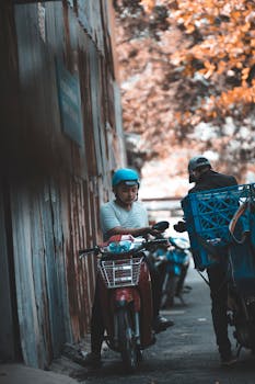 Motorcyclists exchanging items outdoors near a street wall. Urban delivery scene.
