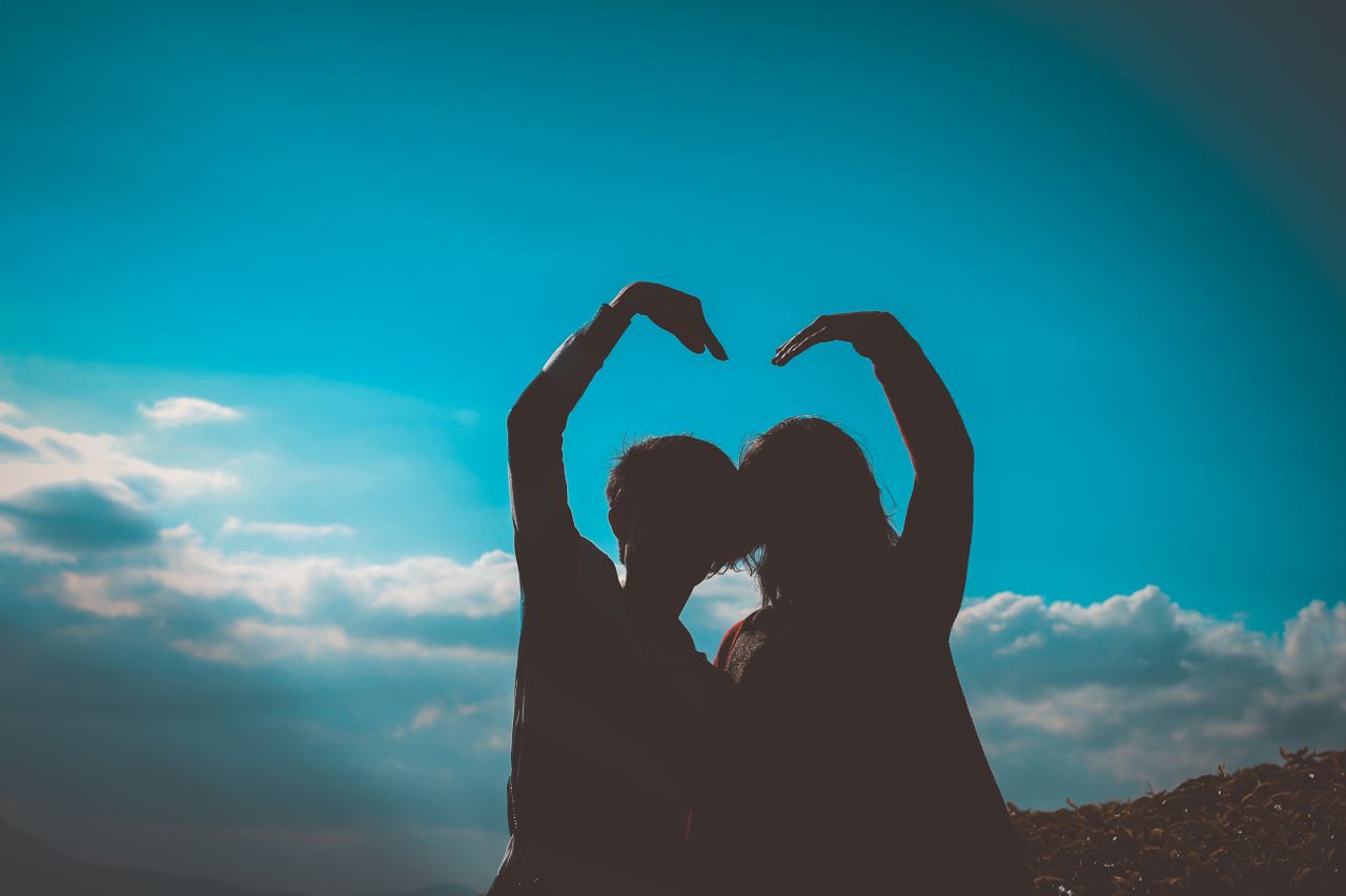 silhouette of a couple creating a heart shape with their arms in a rom