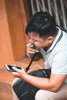 一名男子坐在户外，一边抽烟一边用智能手机，显得既休闲又科技感十足