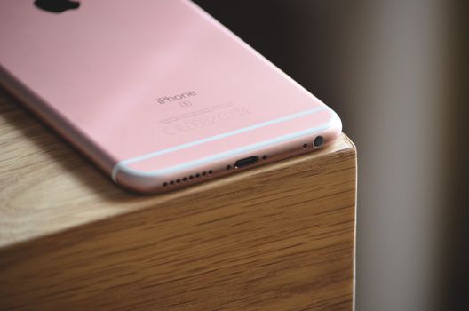 Close-up of a rose gold smartphone resting on a wooden surface. Ideal for technology and lifestyle visuals.