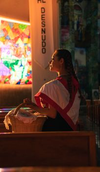 A woman in traditional attire holds a basket in a Mexican church, Huauchinango.