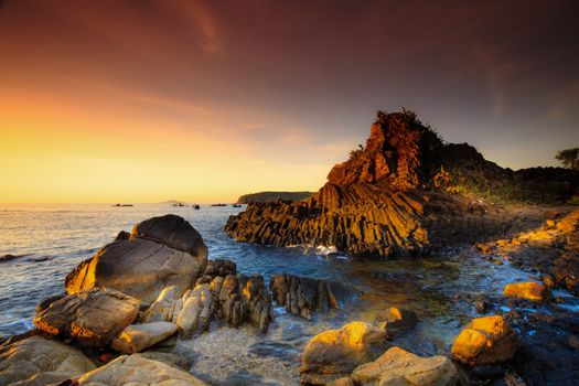 A serene rocky seascape at sunset with golden hues reflecting on the water and rocks, creating a tranquil atmosphere.