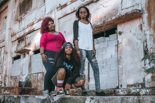 Three young women enjoying togetherness, posing by rustic urban building.