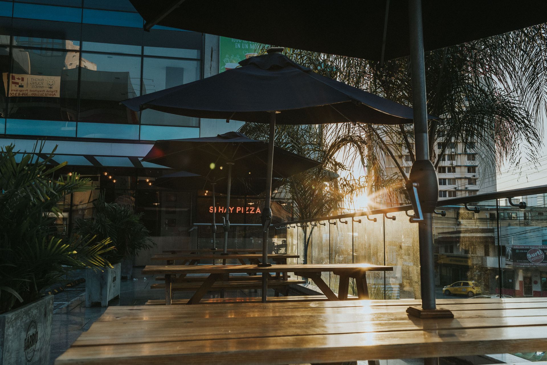Modern outdoor patio with tables and umbrellas in a city setting during sunset.