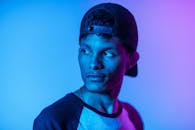 一名戴着帽子的年轻人在戏剧性的蓝紫色灯光下摆出姿势，营造出忧郁而时尚的氛围