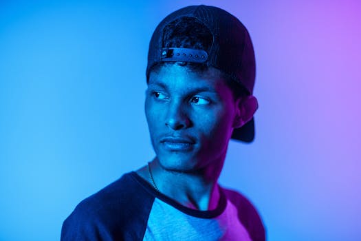 一名戴着帽子的年轻人在戏剧性的蓝紫色灯光下摆出姿势，营造出忧郁而时尚的氛围