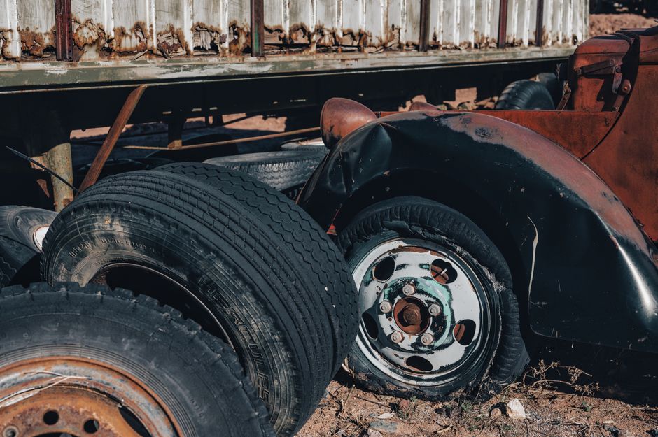 Close-up of rusty vehicle parts and tires in a dusty junkyard setting.