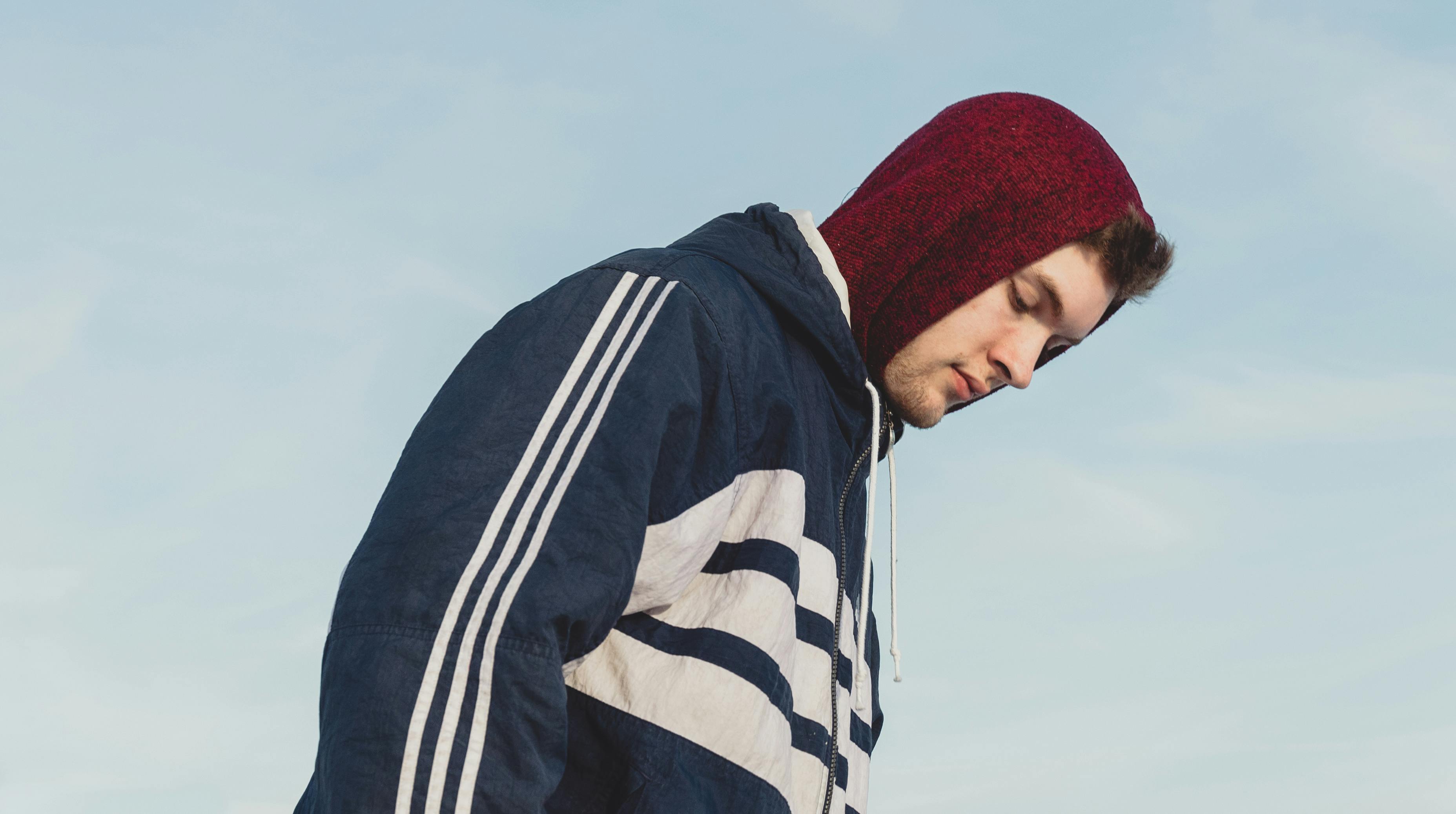 Profile of a young man in a hoodie looking down, set against a clear blue sky.