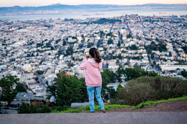 Girl Wearing Pink Hoodie Taking Photo Of City