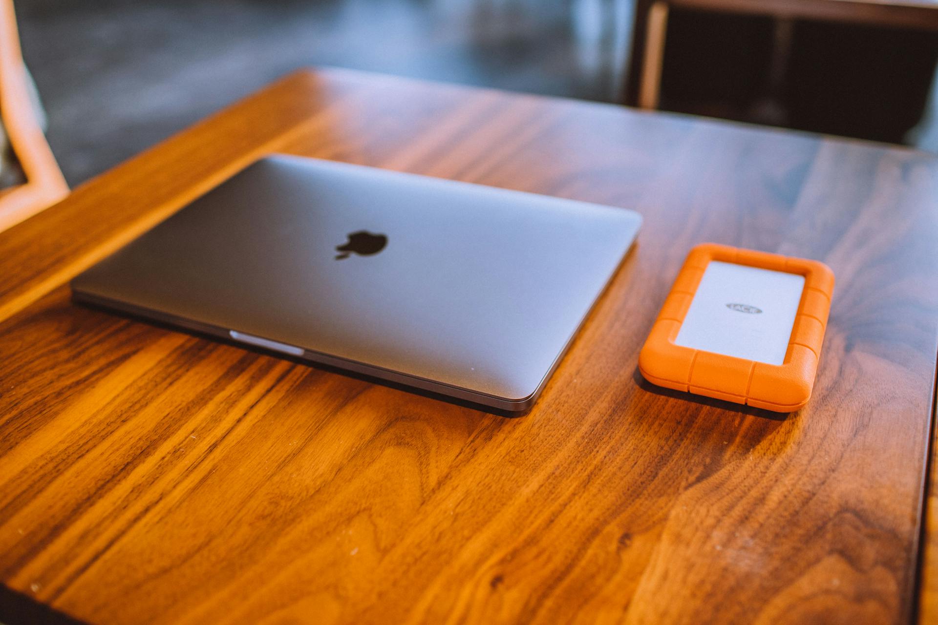 A sleek laptop and rugged external hard drive on a stylish wooden table indoors.