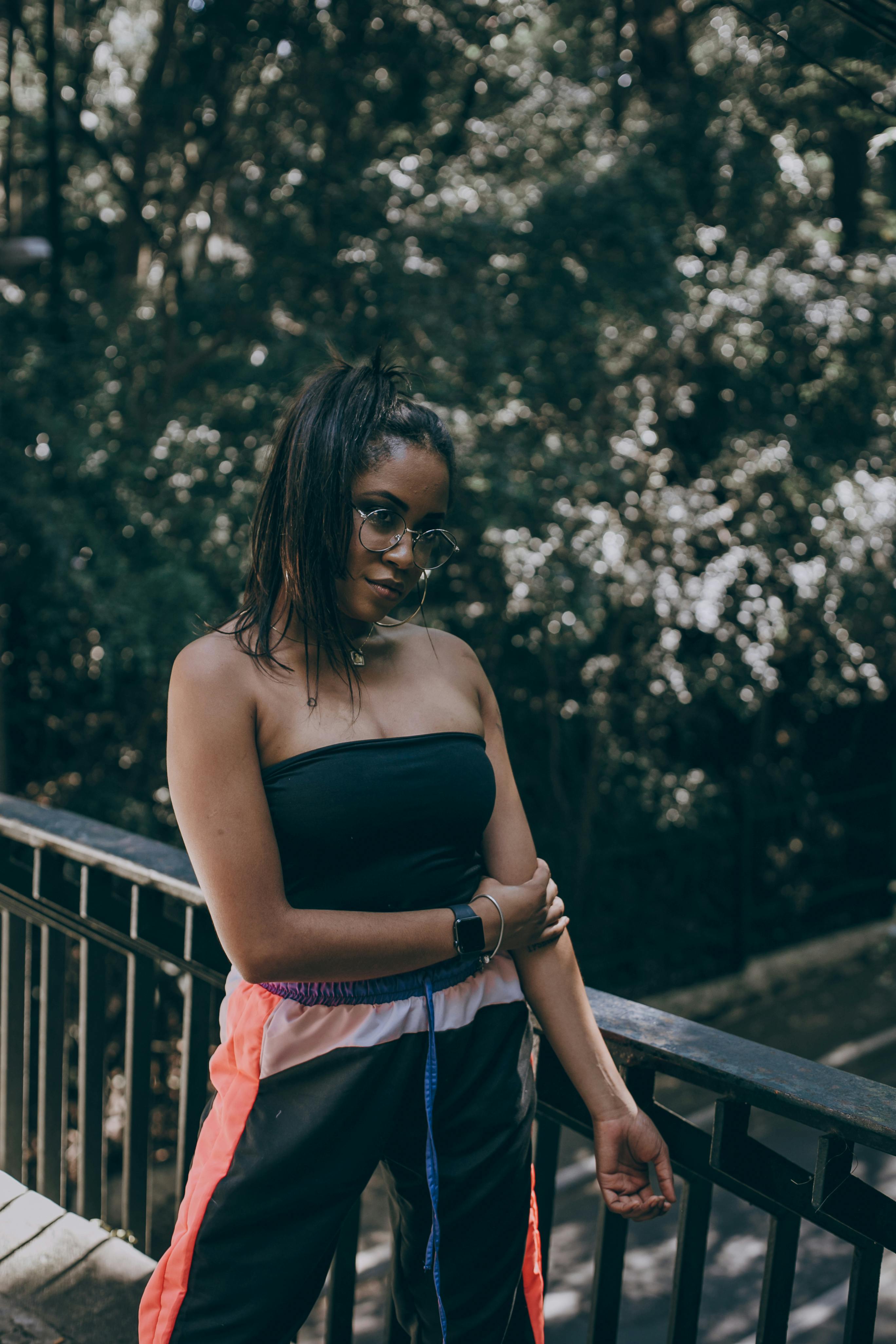 一位时尚女子戴着墨镜，在绿树成荫的桥上摆姿势