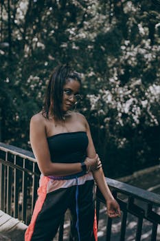 一位时尚女子戴着墨镜，在绿树成荫的桥上摆姿势