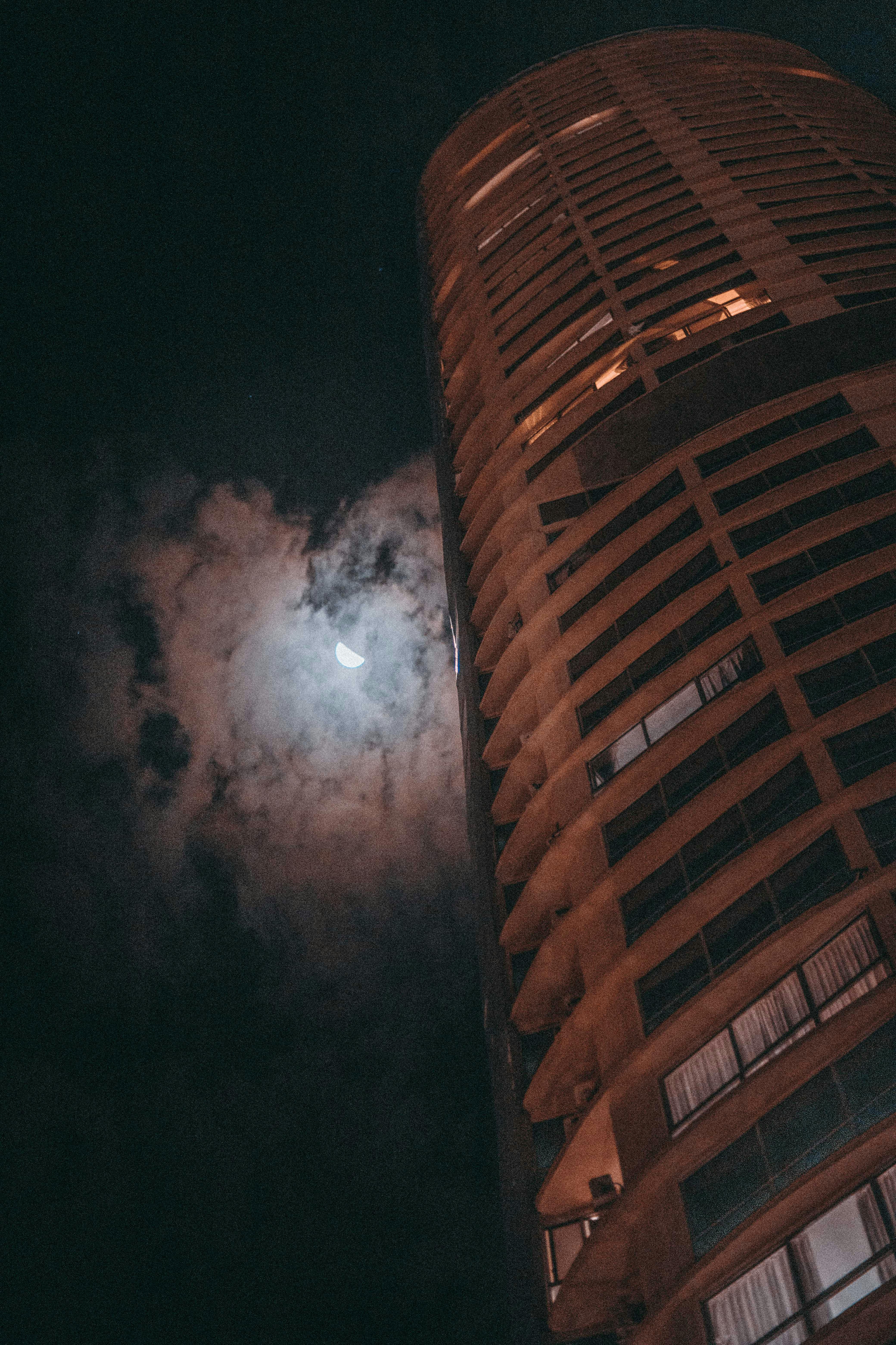 一座高耸的摩天大楼，映衬着夜空、新月和大气云层