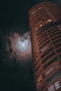 一座高耸的摩天大楼，映衬着夜空、新月和大气云层