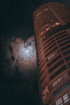 一座高耸的摩天大楼，映衬着夜空、新月和大气云层