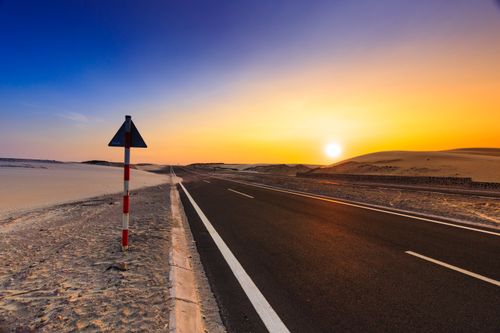 Free A scenic highway in a desert setting at sunset with vibrant skies and sand dunes. Stock Photo