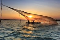 日出时分，渔民在海水中撒网的场景宁静而美丽