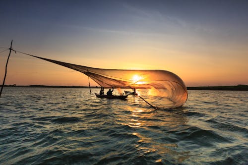 無料 ゴールデンアワーの間にネットで魚を捕まえるボートの男性 写真素材