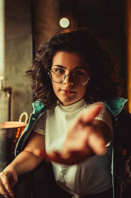 Engaging portrait of a woman with glasses reaching towards the camera indoors.
