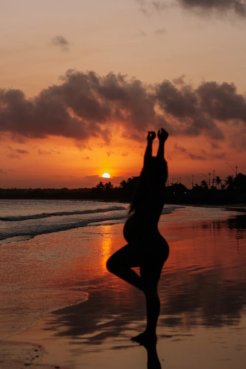 Free A woman doing yoga on the beach at sunset Stock Photo