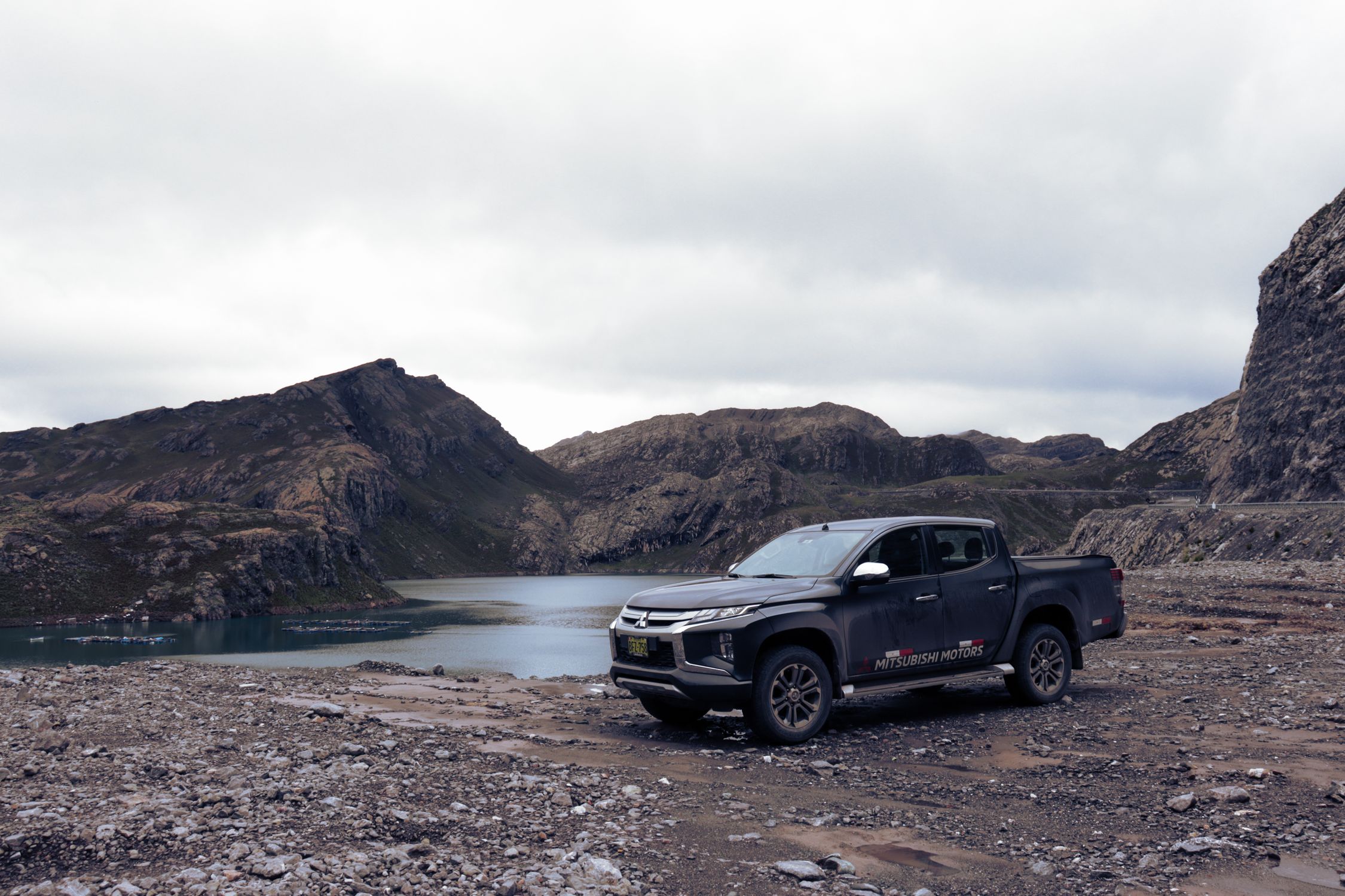 Mitsubishi Triton parked on rugged terrain with a scenic lake and mountains in the background.