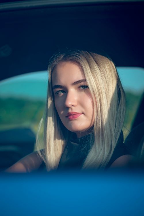 Free Close-up portrait of a blonde woman in a car, capturing natural light and serene expression. Stock Photo