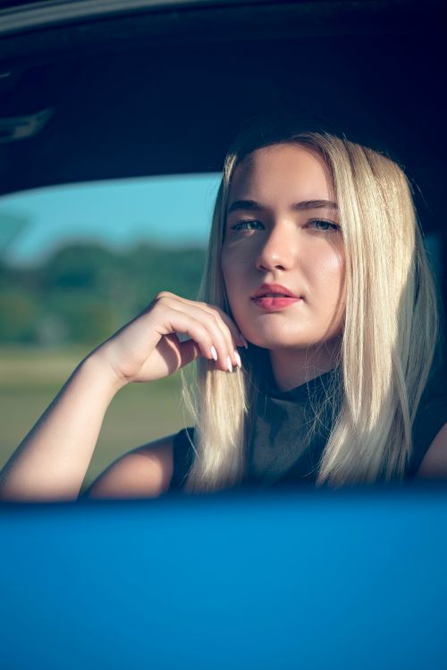 Free A beautiful blonde woman sitting in a car and gazing thoughtfully outside under the daylight. Stock Photo