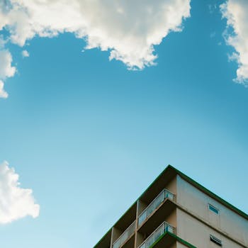 View of an urban apartment building with clouds against a clear blue sky, creating a serene urban landscape.