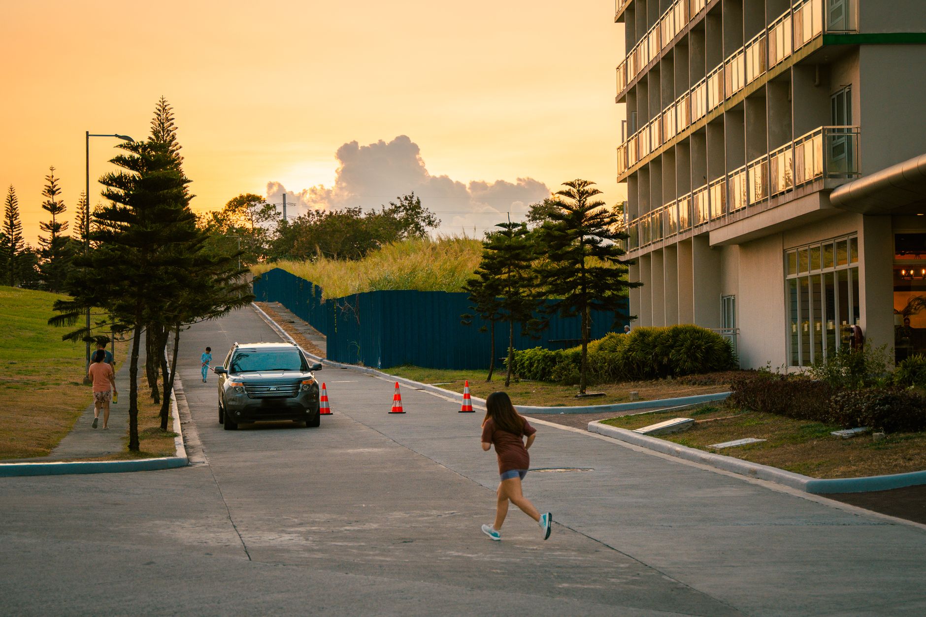 A young girl running down a road next to an apartment building at sunset. Vibrant and lively evening scene.