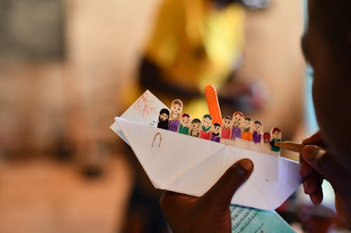 A person holding a paper boat with people on it