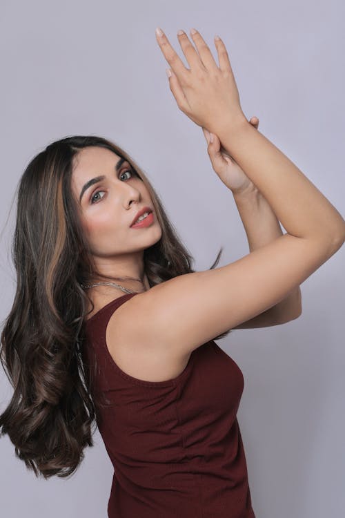 A woman in a maroon top and jeans holding her hand up