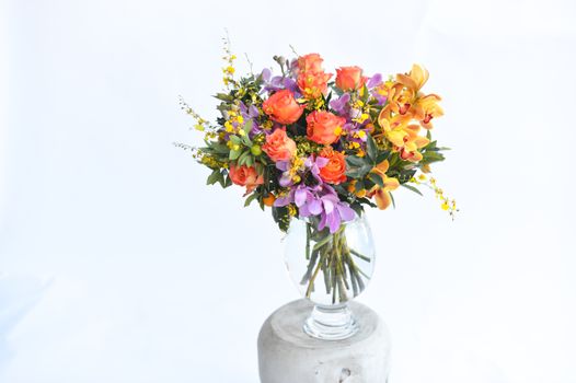 A colorful flower arrangement featuring roses and orchids in a clear glass vase on a light background.