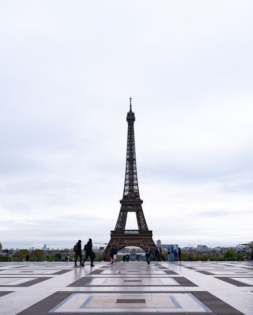 Free View of the Eiffel Tower with people in Paris, capturing the iconic landmark under a cloudy sky. Stock Photo