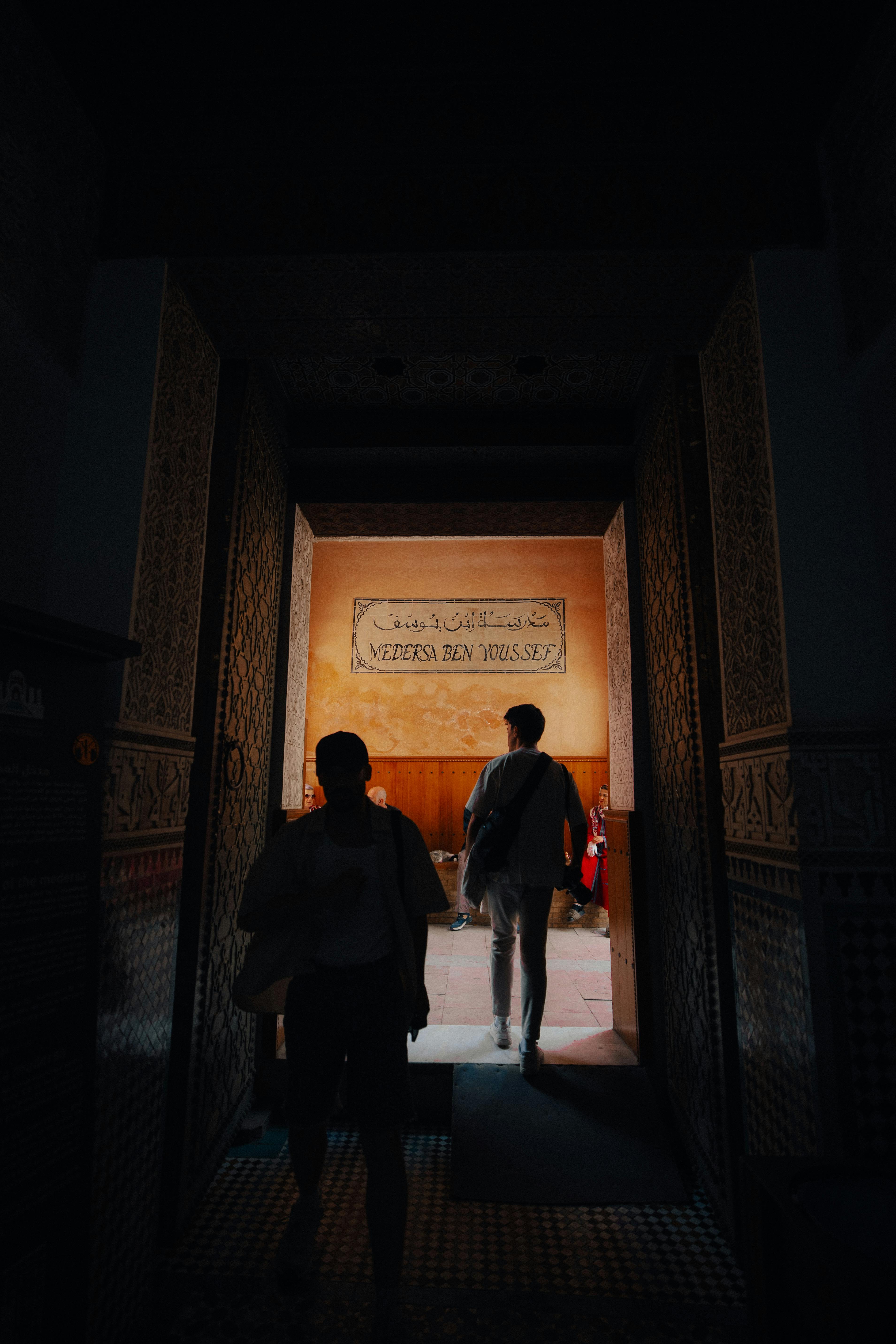 Two people silhouetted in an ornate, historic doorway leading to a well-lit interior.