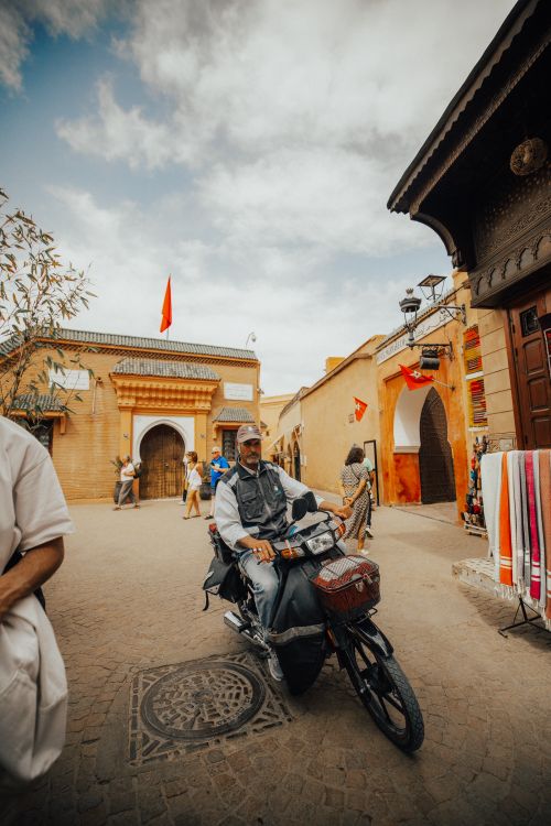 Free Man riding a motorbike on a lively street in Morocco, showcasing traditional architecture and culture. Stock Photo