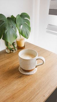 A serene coffee cup setting with Monstera plant on wooden table.