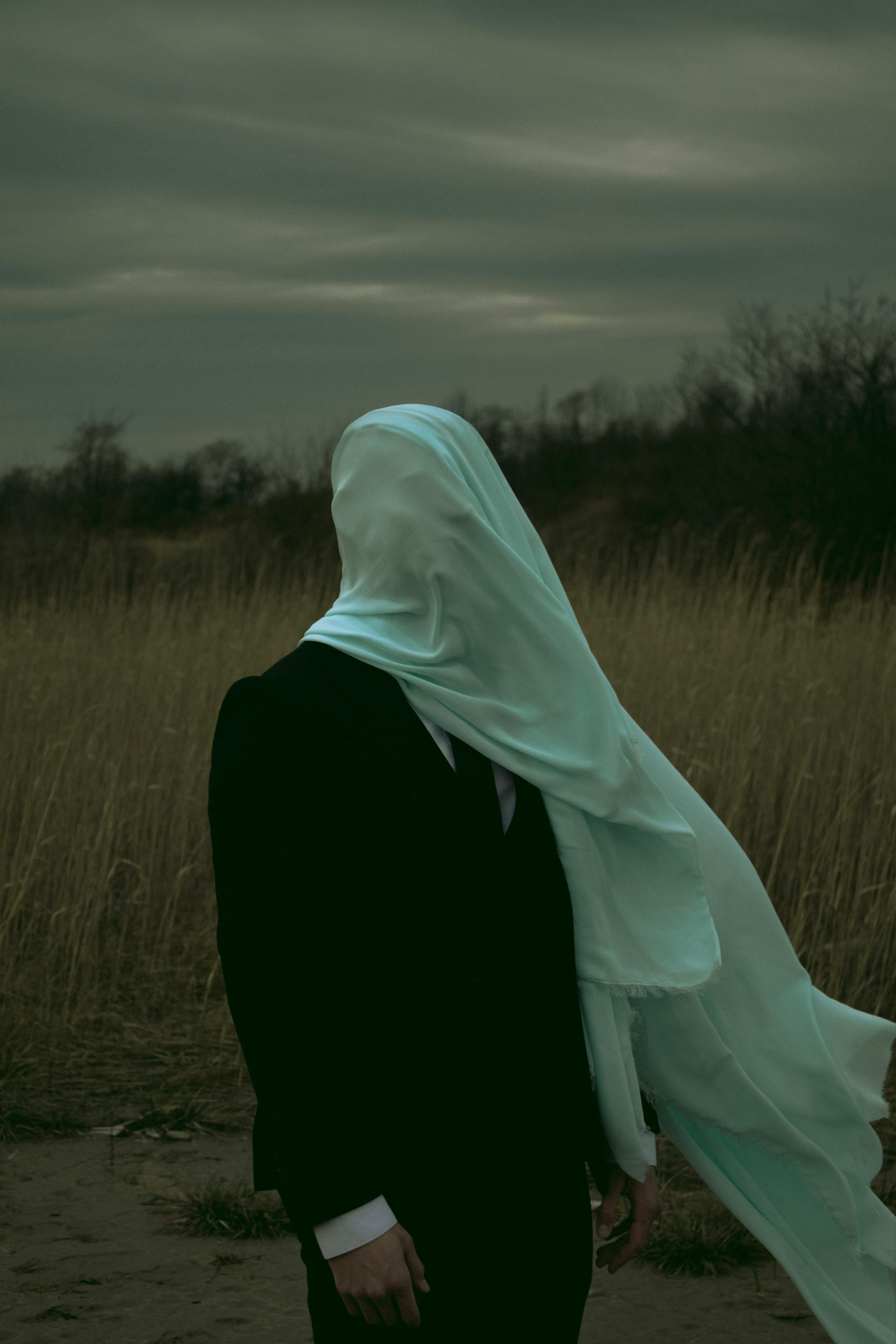 An enigmatic figure in a suit with a veil in an open field creates a mysterious atmosphere.