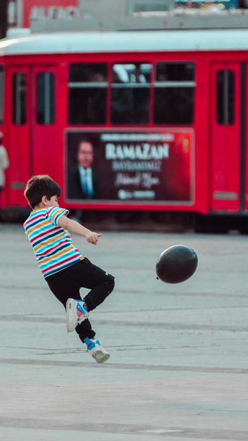 A boy kicking a soccer ball in front of a bus