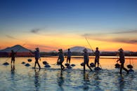 日落时分，农民们在宁静的水景中收割盐，身影在充满活力的余晖下映成剪影