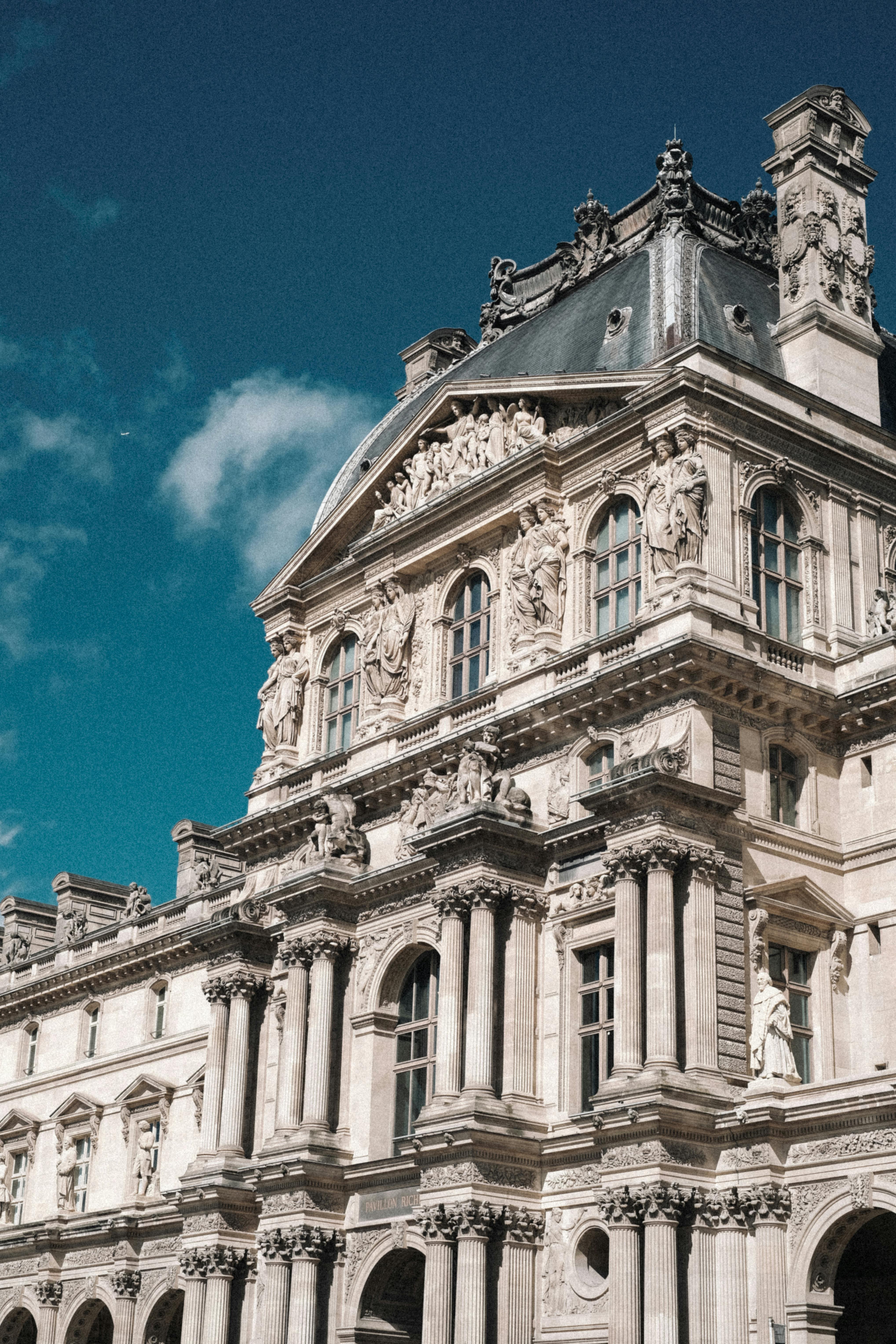 Elegant facade of the Louvre Museum under a bright blue sky in Paris, France.