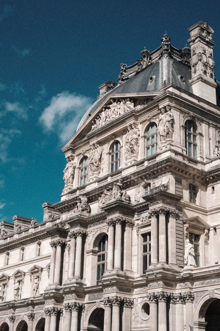 Elegant facade of the Louvre Museum under a bright blue sky in Paris, France.