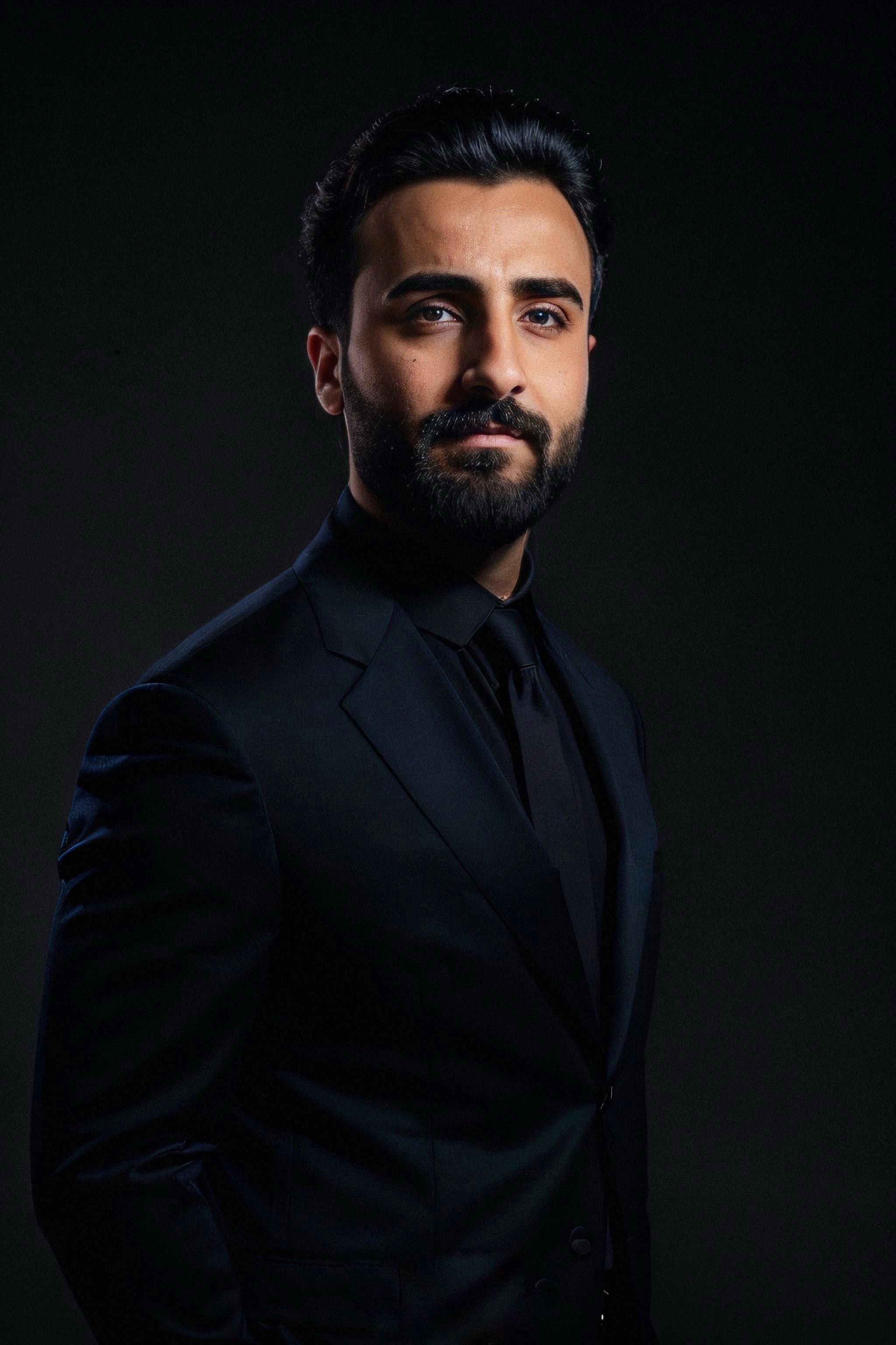 Professional portrait of a bearded man in a black suit, studio setting.