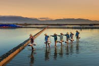 日落时分，农民在宁静的水边收割盐，水面倒映着他们的身影